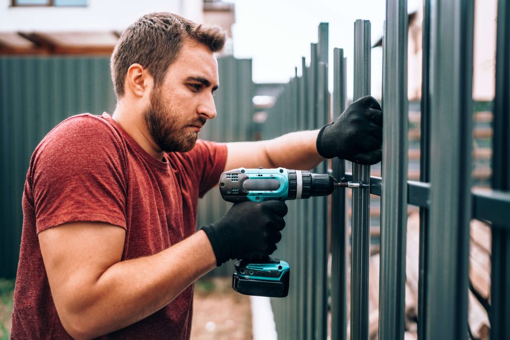 man building a metal fence with power drill