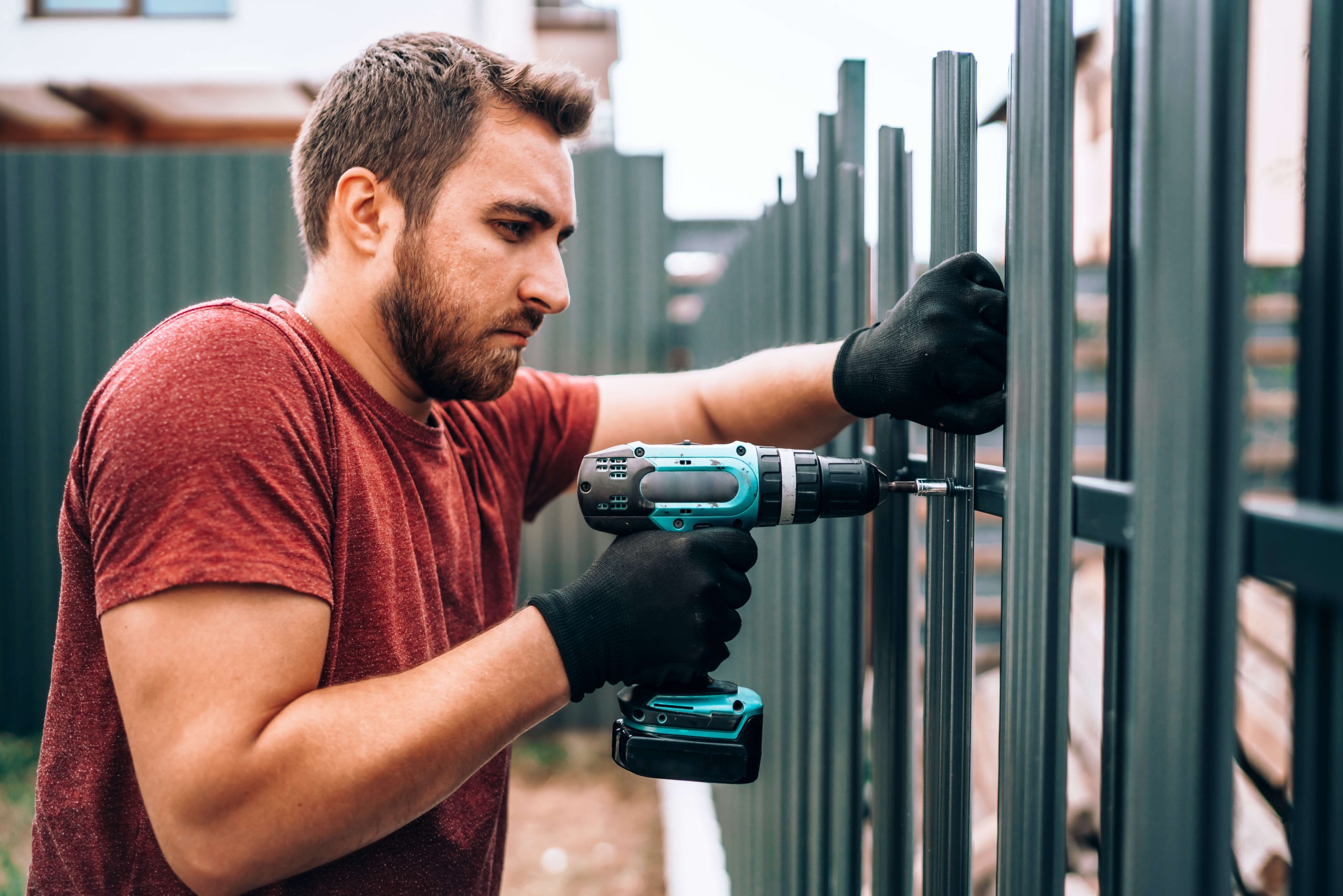 man building a metal fence with power drill