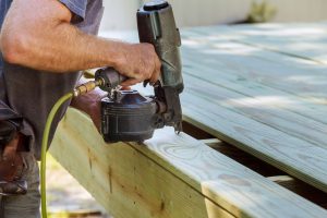 man installs wooden deck with power drill