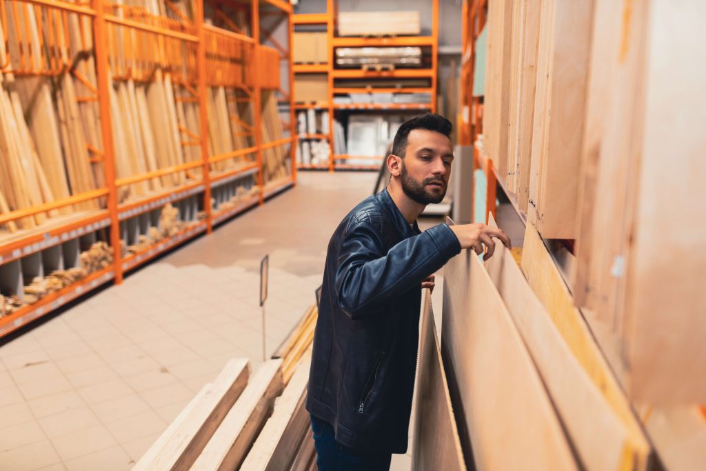 brunette man in leather jacket looking through plywood at the hardware store
