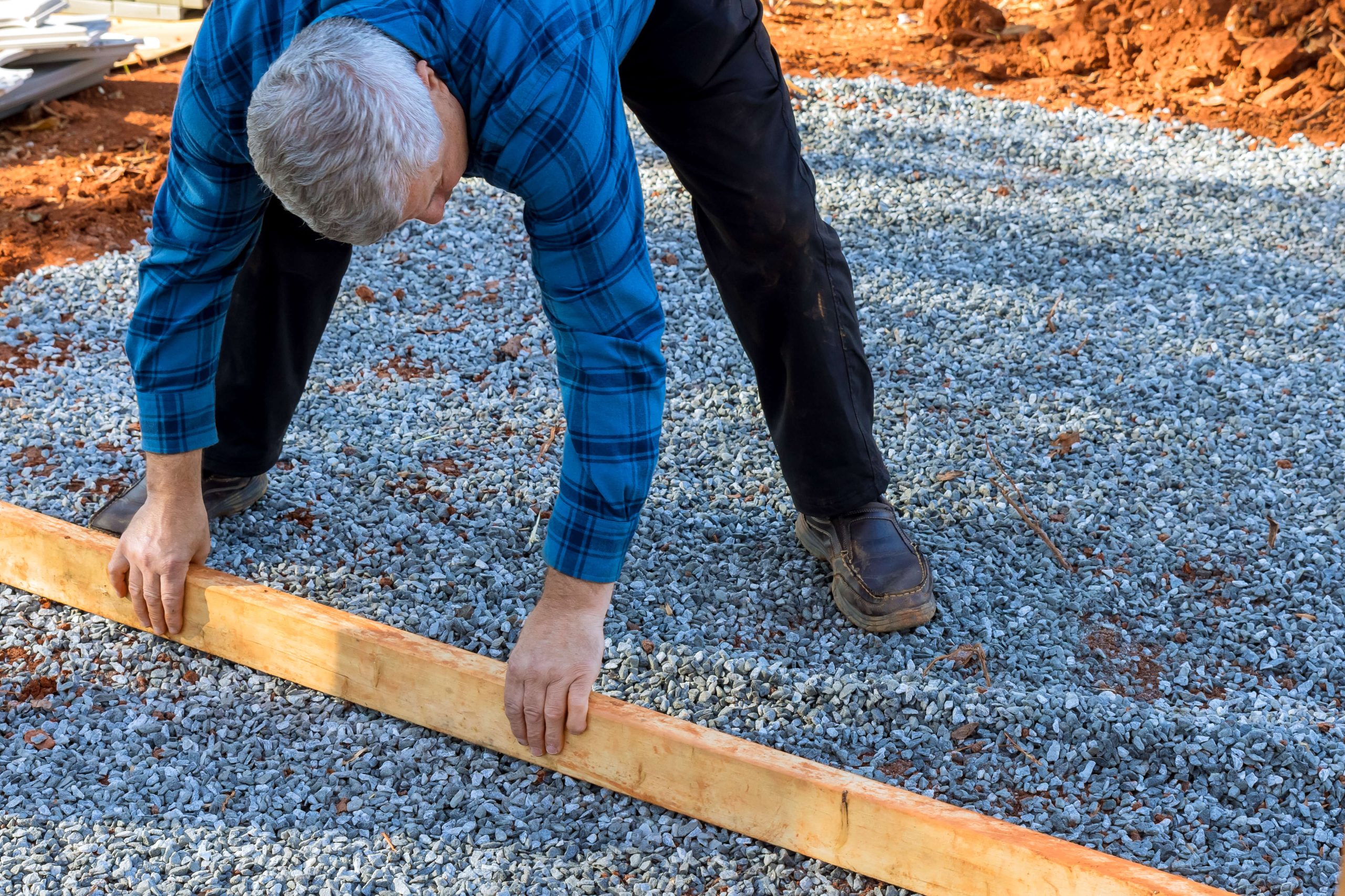 older man in blue flannel shirt building the deck foundation for a backyard shed