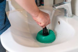 man unclogging bathroom sink with a plunger