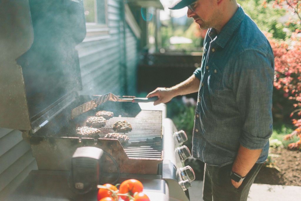 man outdoors using a gas grill to make burgers