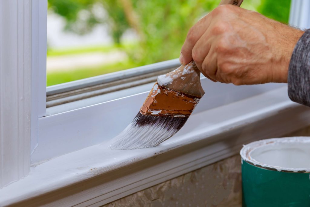 closeup shot of person using a paint brush to paint white trim on window
