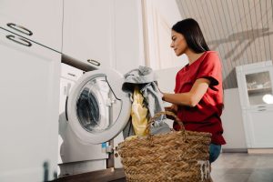 yong woman at hme putting clothes into the washing machine