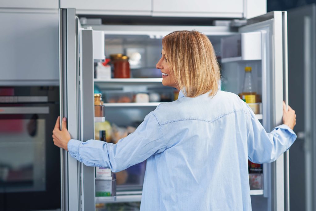 blonde woman smiling in front of open fridge